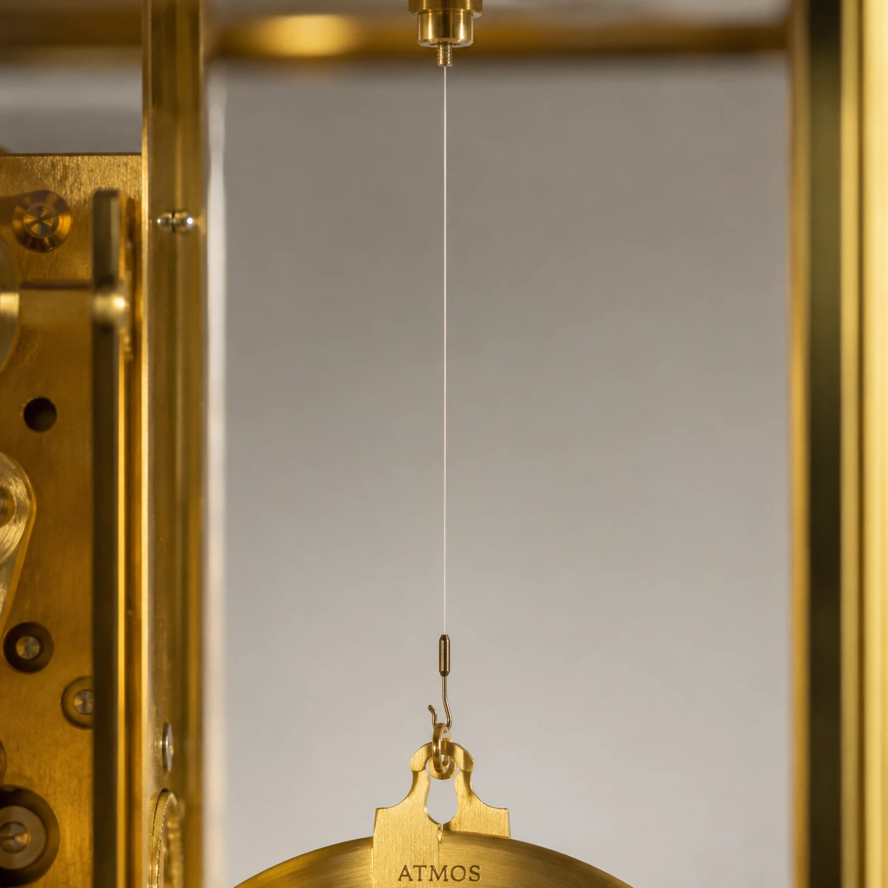 Gros plan du fil de suspension et du balancier annulaire d'une pendule Atmos